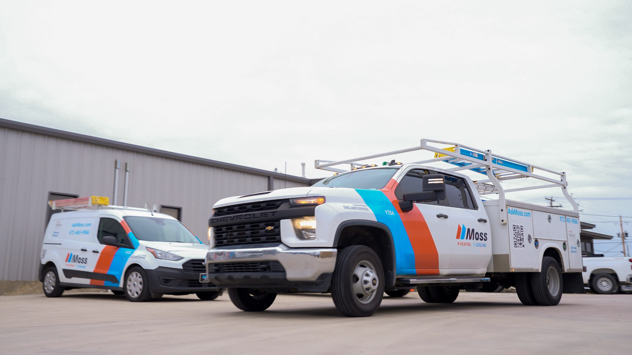 Service trucks with blue/orange Moss branding parked by a metal building; HVAC company vans ready for work.