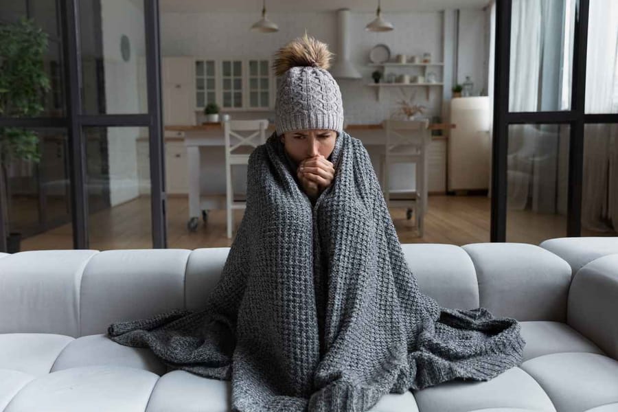Woman sitting on a couch wrapped in a blanket because her heater is not working