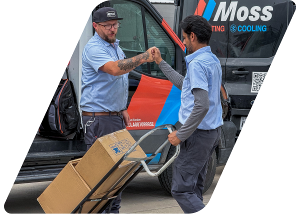Two delivery workers fist bump beside a Moss Cooling van, one pushing a dolly loaded with boxes.