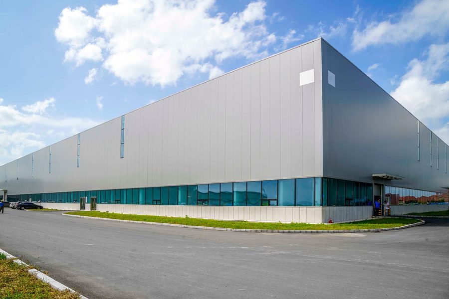 Large gray metal warehouse with glass storefront along the bottom edge under a blue sky.