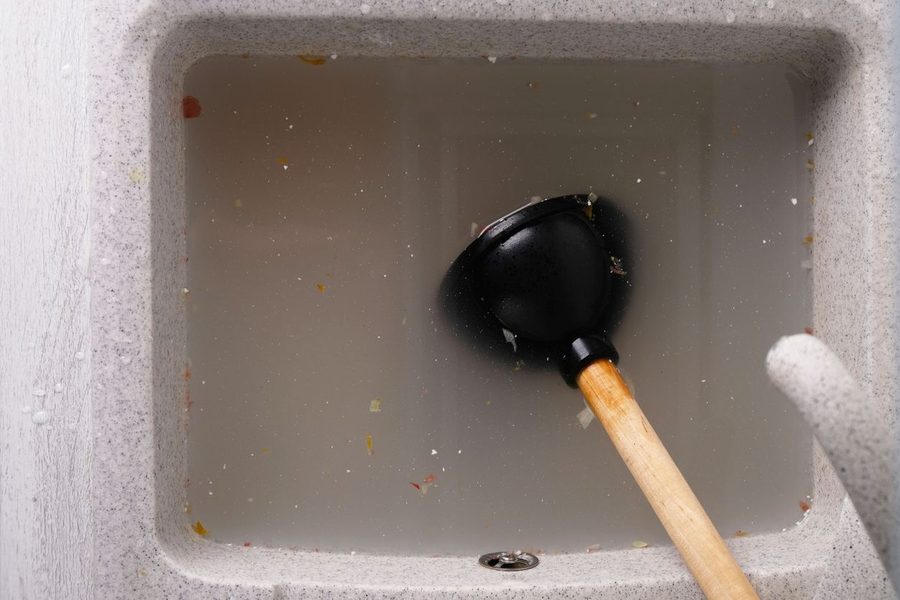 plunger with wooden handle lies in clogged sink in water, removing blockage