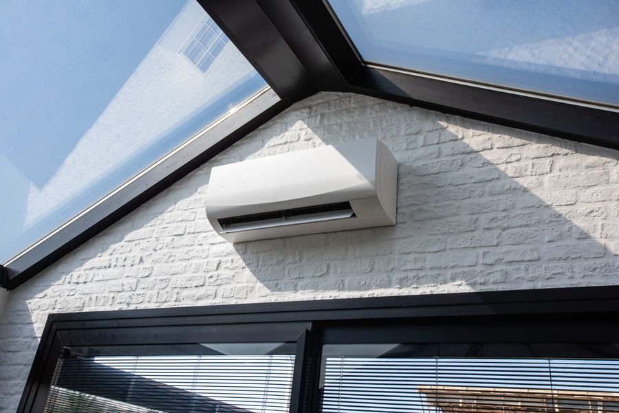 White wall-mounted air conditioner unit installed on a white brick wall beneath a glass skylight/roof.