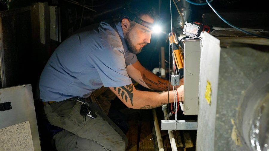 technician working on a furnace with a headlamp