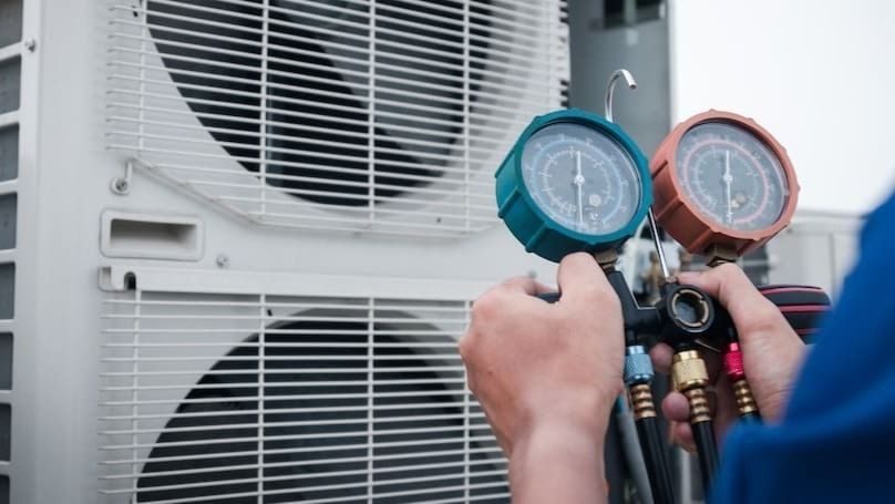 Technician using a refrigerant manifold gauge set on an outdoor HVAC unit to measure pressures.