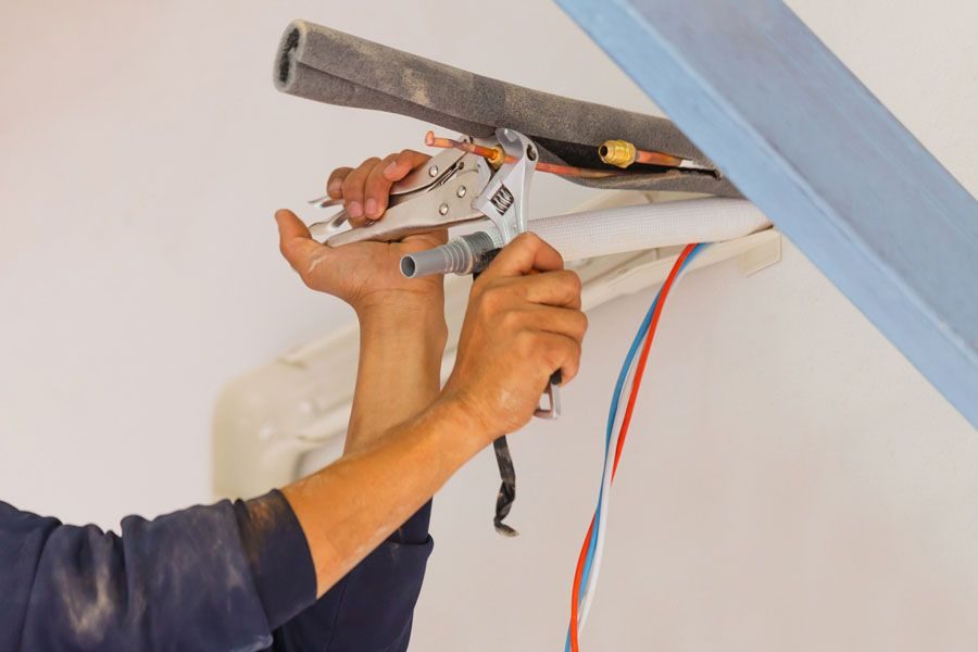 Close-up of a worker connecting electrical wires with a crimping tool, red, blue, and white conductors visible in a wall cavity