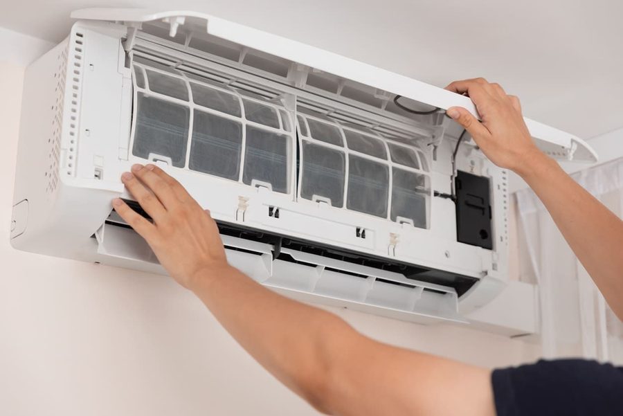 Hands open the front panel of a wall-mounted split air conditioner to access its filter for cleaning/maintenance.