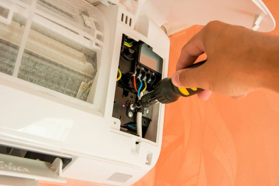 Close-up of a hand using a screwdriver to access the interior of a white electronic device with exposed wiring and circuit components.