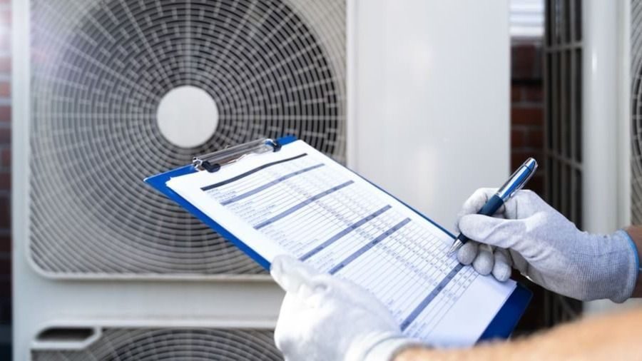 HVAC technician wearing gloves writing on an inspection clipboard in front of outdoor air conditioner units