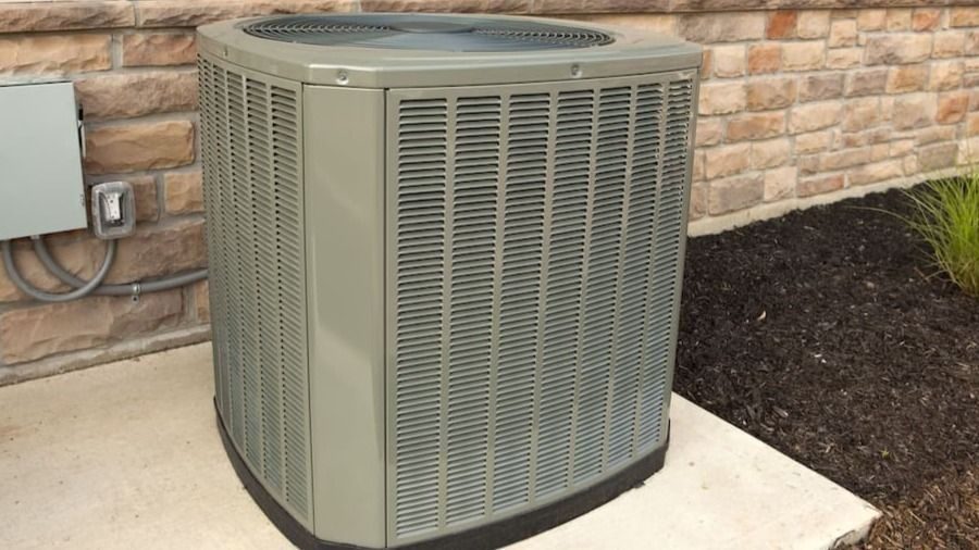 Outdoor air conditioning condenser unit on a concrete pad beside a brick wall