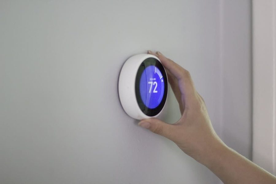 Hand adjusting a round wall thermostat set to 72°F, mounted on a light-gray wall
