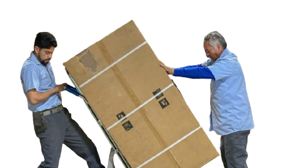 Two men in blue shirts push a large cardboard box on a dolly, one at each end.