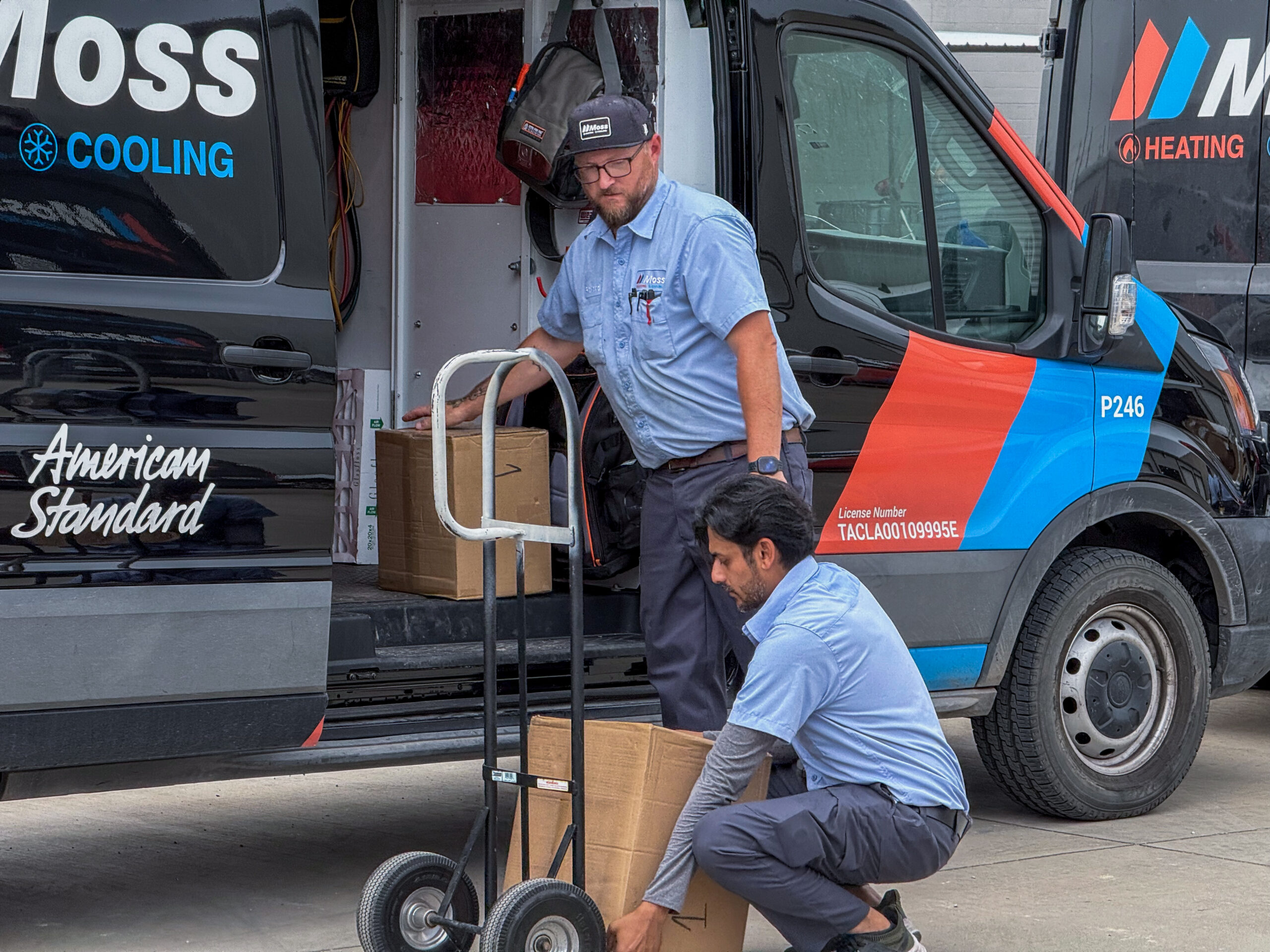 Service technician unloading cardboard boxes from a Moss Cooling/Heating van using a hand truck.