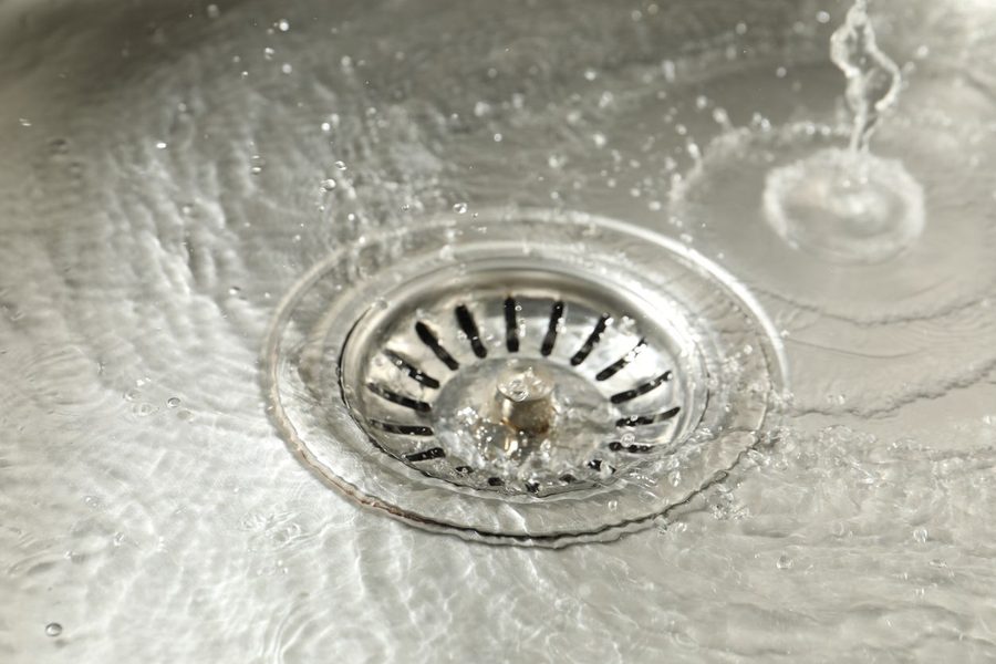 Close-up of a stainless steel sink drain with water swirling around and droplets splashing nearby.