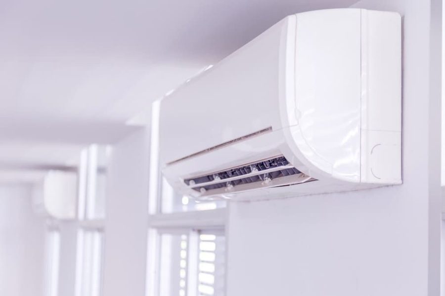 White wall-mounted air conditioner with its vent open, mounted high on a bright wall in a minimalist room.