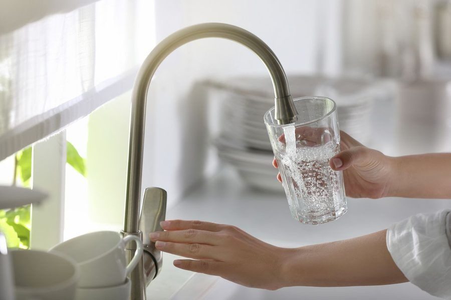 Person fills a clear glass with water from a curved stainless-steel kitchen faucet at a sink